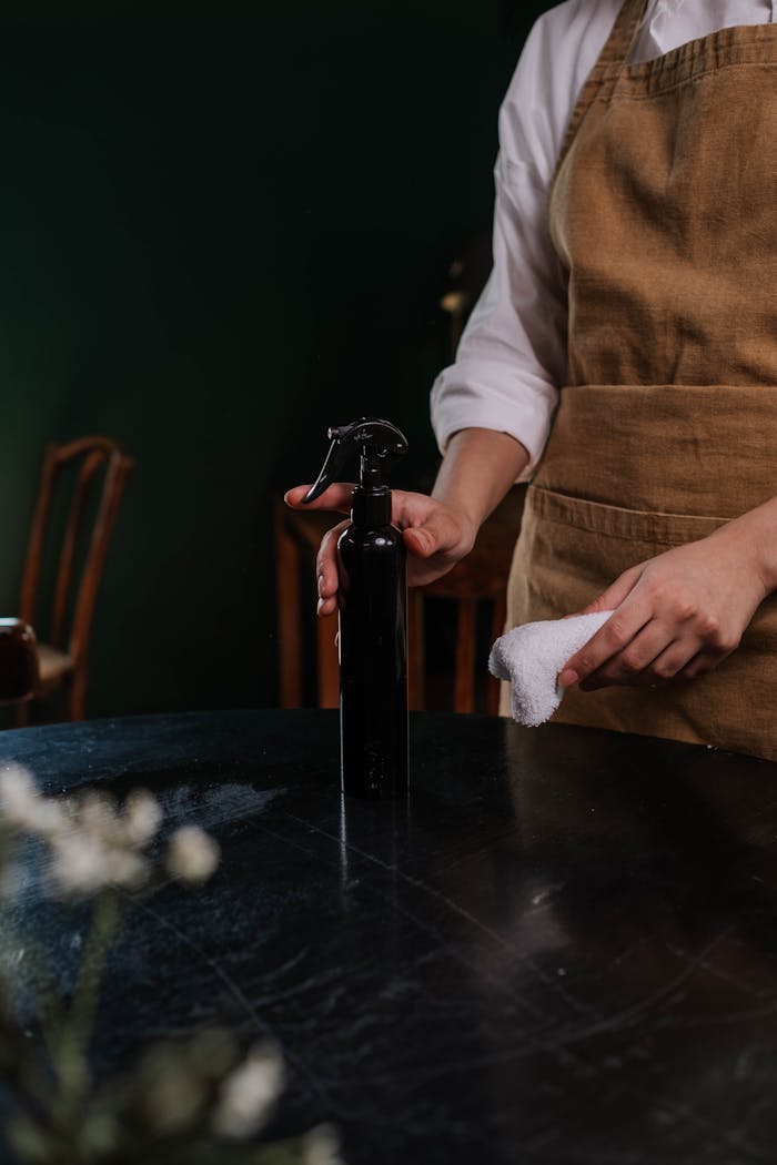 services-01 A waitress in an apron cleaning a table with a spray bottle and cloth in a dimly lit restaurant.